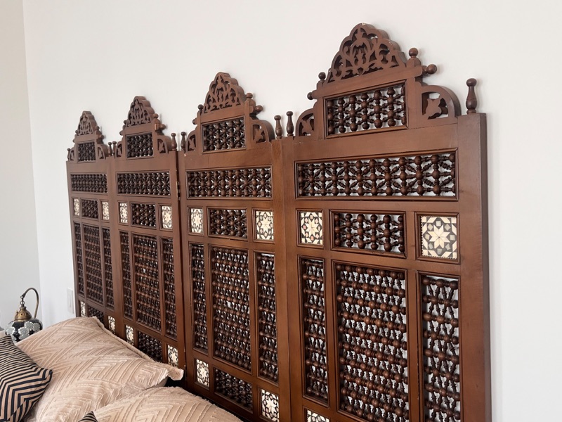 A four-panel folding mashrabiya screen standing against a wall, its lattice made of hundreds of turned wooden spindles.