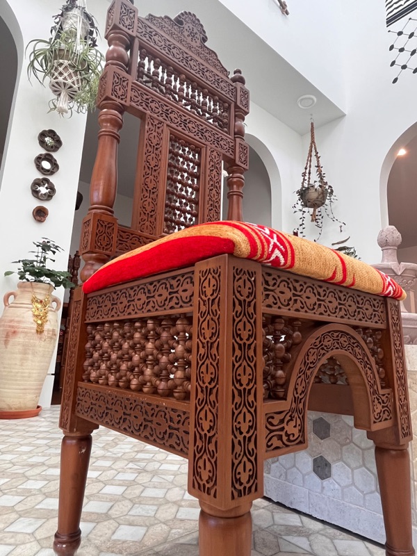 A single chair photographed close, showing the horseshoe arch beneath the seat and the depth of the relief carving.