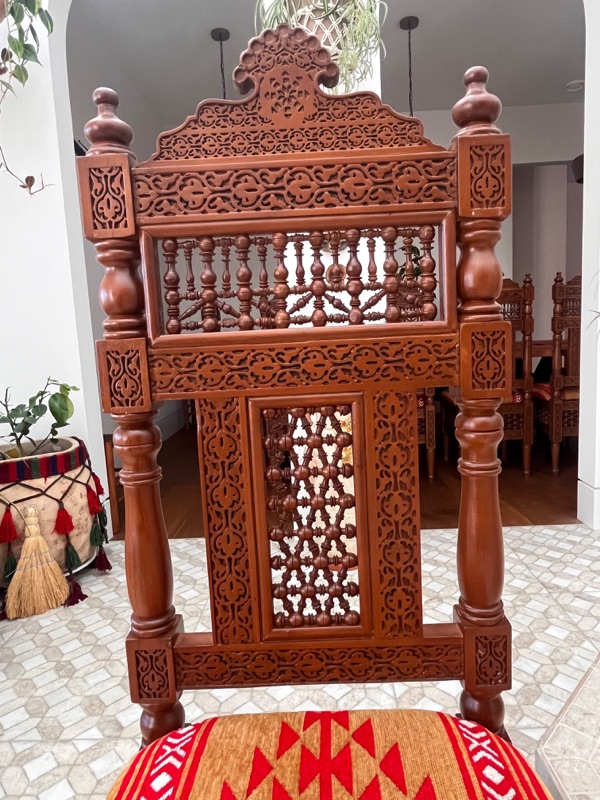The carved crest at the top of a chair back, cut into a scalloped arch.