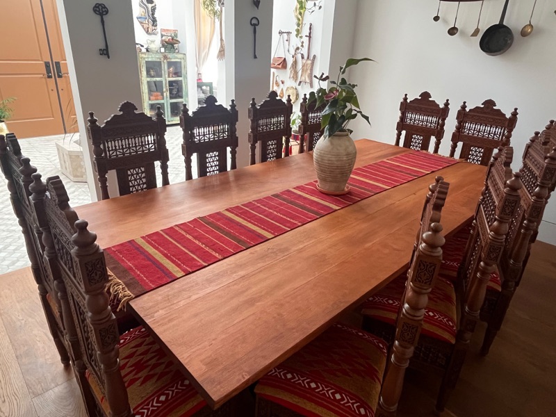The full dining set seen from one end, twelve carved chairs around a solid-wood table with a striped runner.