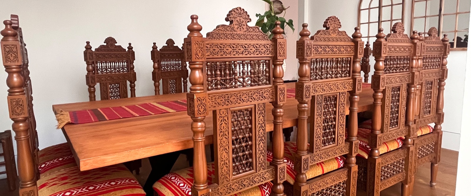 A hand-carved Arabesque dining set for twelve, the chairs showing turned-spindle mashrabiya panels and deep relief carving, in a client's dining room.